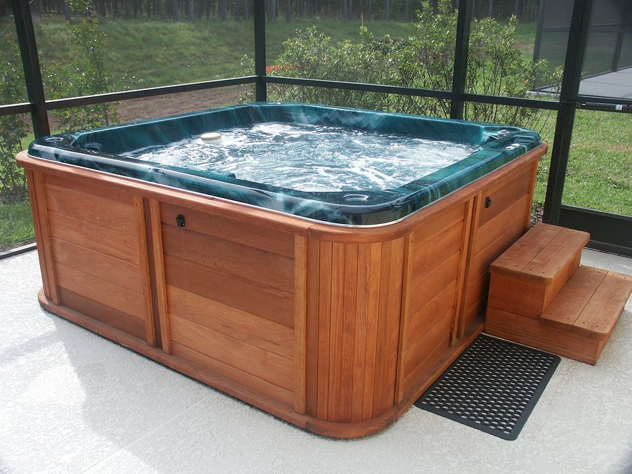 Wood-paneled above-ground hot tub with bubbling water inside a screened patio enclosure