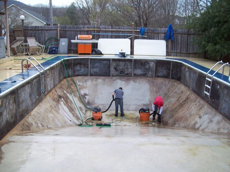 Two workers vacuum and clean the bottom of an empty in-ground pool after the old vinyl liner has been removed.