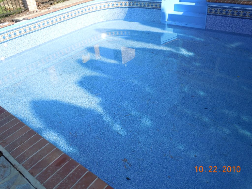 Shallow end of an in-ground pool with blue vinyl liner, entry steps, and light ripples on the water.