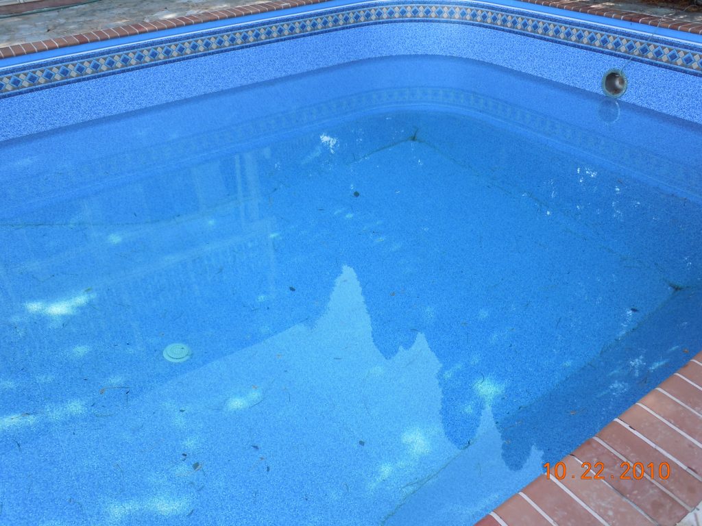 Close-up of a blue patterned vinyl pool liner underwater, showing the shallow floor and waterline tile border.