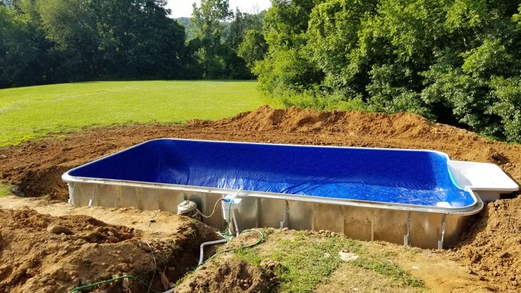 Rectangular in-ground pool during installation with a new blue vinyl liner in place and water filling inside, surrounded by excavated soil.