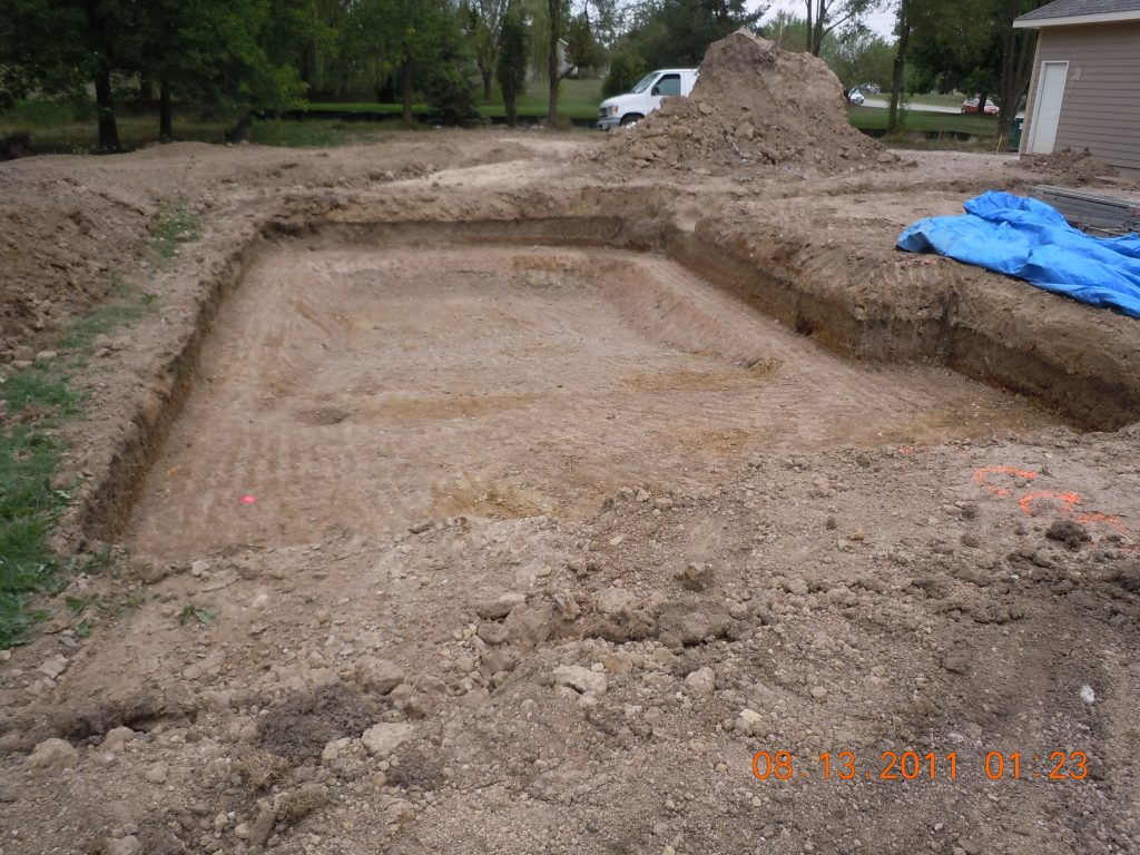 Excavated rectangular in-ground pool area during early construction, with dirt pile and tarp nearby.