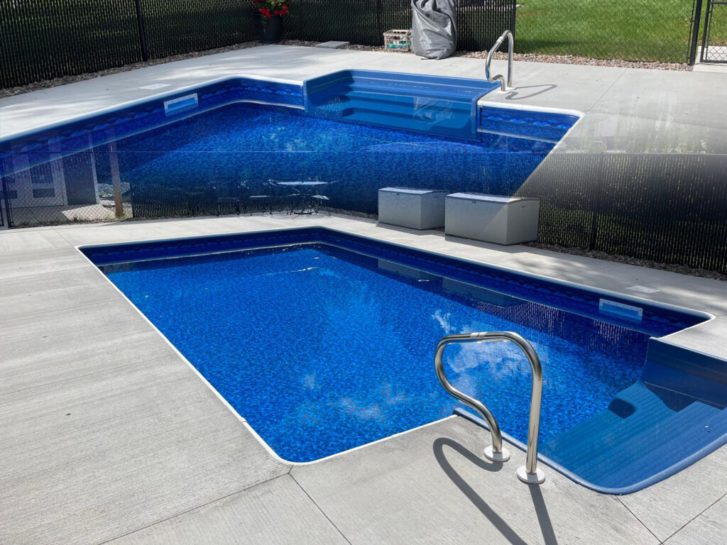 Rectangular in-ground pool with bright blue vinyl liner, shallow-end steps, and concrete deck.